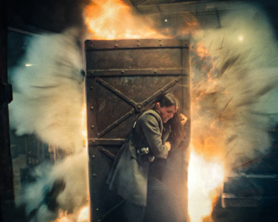 이미지는 영화 **《발레리나》**의 스틸컷입니다. 주인공인 루니(아나 데 아르마스)가 폭발하는 문을 힘겹게 막아서고 있는 장면입니다. 주변으로 불꽃과 연기가 뿜어져 나와 매우 긴박하고 위험한 상황임을 보여주며, 영화 속에서 그녀가 겪게 될 치열한 액션과 위기를 엿볼 수 있습니다.