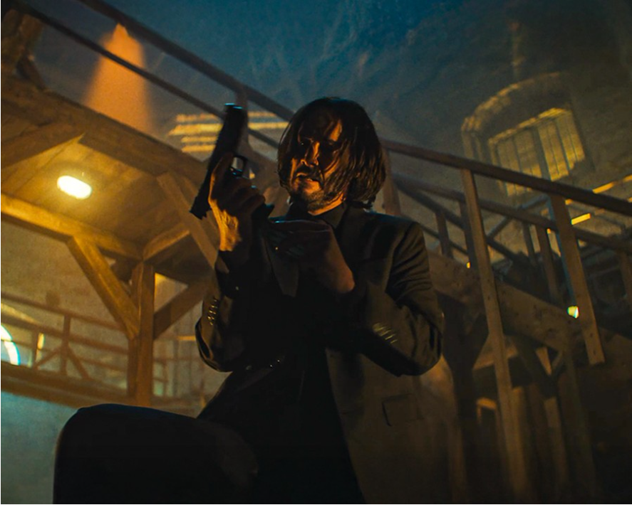 이미지는 영화 **《발레리나》**의 스틸컷입니다. 키아누 리브스가 연기하는 존 윅이 어두운 공간에서 권총을 손에 든 채 어딘가를 응시하고 있습니다. 아래에서 비추는 조명은 그의 얼굴에 그림자를 드리워 긴장감과 결연한 분위기를 강조하며, 영화 속 액션 장면의 일부임을 보여줍니다.