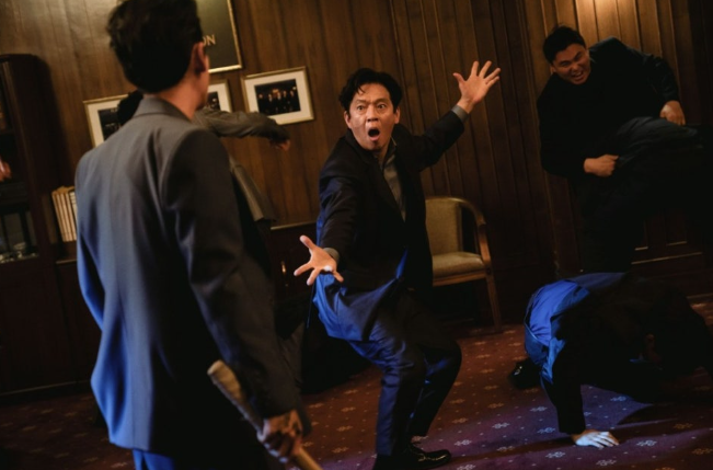 영화 **'보스(BOSS)'**에서 배우 박지환이 연기하는 캐릭터가 일촉즉발의 난전 속에서 당황한 기색을 감추지 못하는 코믹한 순간을 담고 있습니다.